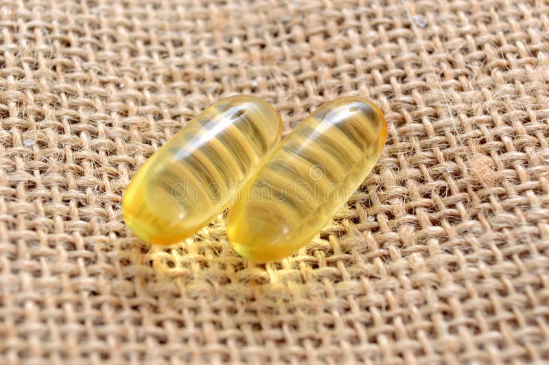 Capsules van het de olie de omega 3 gel van de kabeljauwlever op zakachtergrond stock fotografie Capsules van het de olie de omega 3 gel van de kabeljauwlever op zakachtergrond stock fotografie