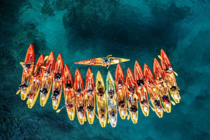 Captain of the kayaking team stands perpendicular in the boat in front of a row of kayaks. Top view