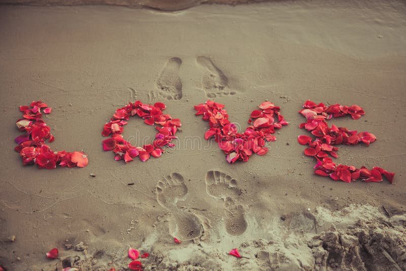 Caption word love in the sand of the sea. Love inscription from the petals of roses.