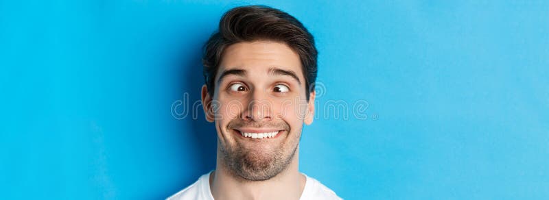 Captura de cabeza de un joven haciendo expresiones graciosas sonriendo y escupiendo sobre fondo azul fotos de archivo libres de regalías