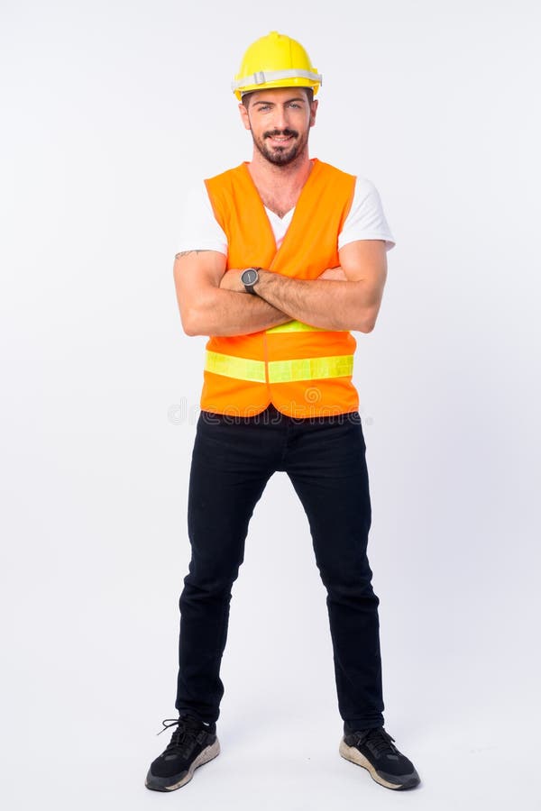 Captura de cuerpo entero del joven feliz hombre barbudo trabajador de la construcción sonriendo con los brazos cruzados imagen de archivo Captura de cuerpo entero del joven feliz hombre barbudo trabajador de la construcción sonriendo con los brazos cruzados imagen de archivo