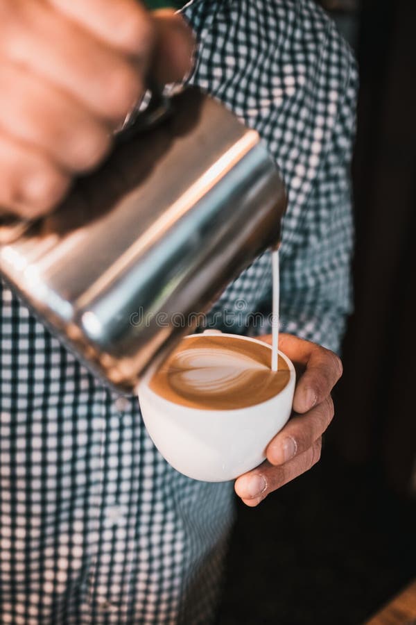 Captura vertical de un hombre vertiendo leche espumosa en una taza de capuchino.