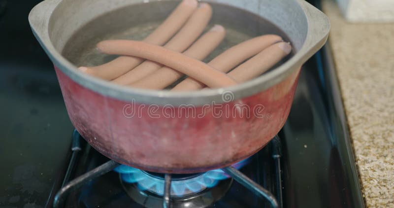 Capture d'écran de saucisses bouillantes dans une casserole sur une cuisinière à gaz banque de vidéos