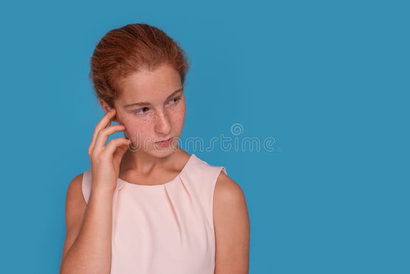 Capture d'écran d'une adolescente séduisante aux cheveux rouges réfléchissant à quelque chose sur fond bleu photographie stock libre de droits Capture d'écran d'une adolescente séduisante aux cheveux rouges réfléchissant à quelque chose sur fond bleu photographie stock libre de droits