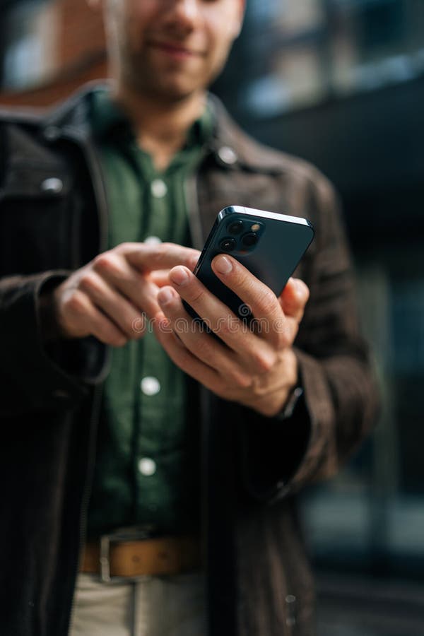 Capture d'écran verticale sélective d'un homme méconnaissable tenant et utilisant un smartphone debout sur la route de la ville images stock