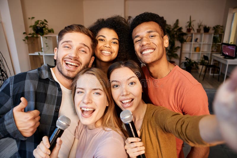 Capture the moment. Cheerful young multicultural friends taking a selfie using smartphone while spending time together, playing karaoke at home. Friendship, people, leisure concept