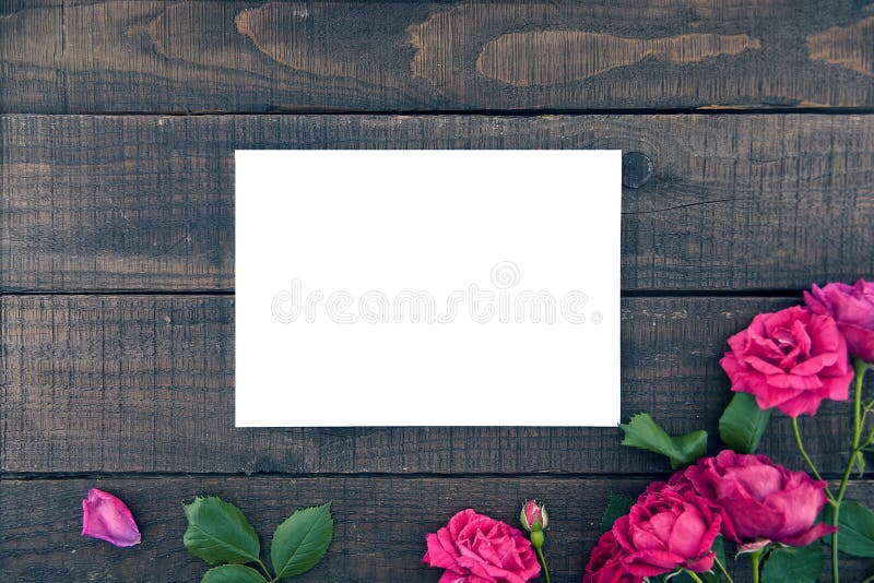 Frame of roses on dark rustic wooden background with empty card for greeting message. Valentine's Day and Mother's Day background. Holiday mock up. Top view. Frame of roses on dark rustic wooden background with empty card for greeting message. Valentine's Day and Mother's Day background. Holiday mock up. Top view.