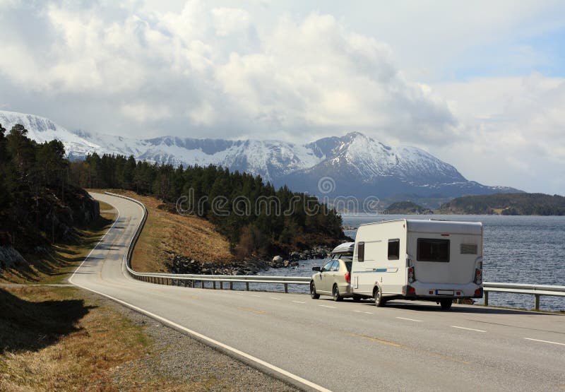 Auto s caravan jazdy na pobrežnej ceste pod horami.