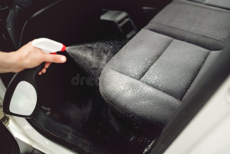 Car care concept, detailing and cleaning car interiors. Worker spraying cleaning solution on car upholstery