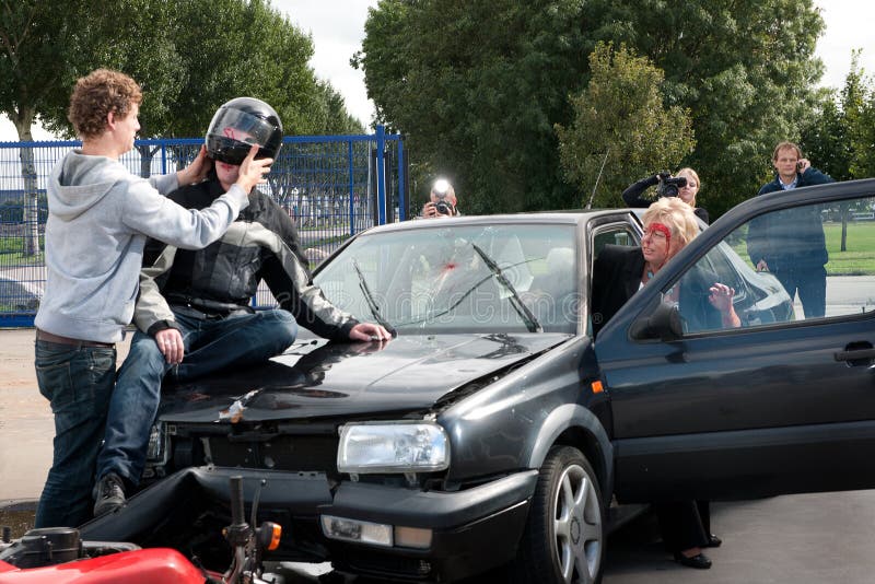 Various things happening just after an accident between a motorcycle and a car. The driver is rushing out of her car to check on the motorist, whose helmet is carefully removed by a bystander. Other bystanders are calling 911, and taking pictures. Various things happening just after an accident between a motorcycle and a car. The driver is rushing out of her car to check on the motorist, whose helmet is carefully removed by a bystander. Other bystanders are calling 911, and taking pictures