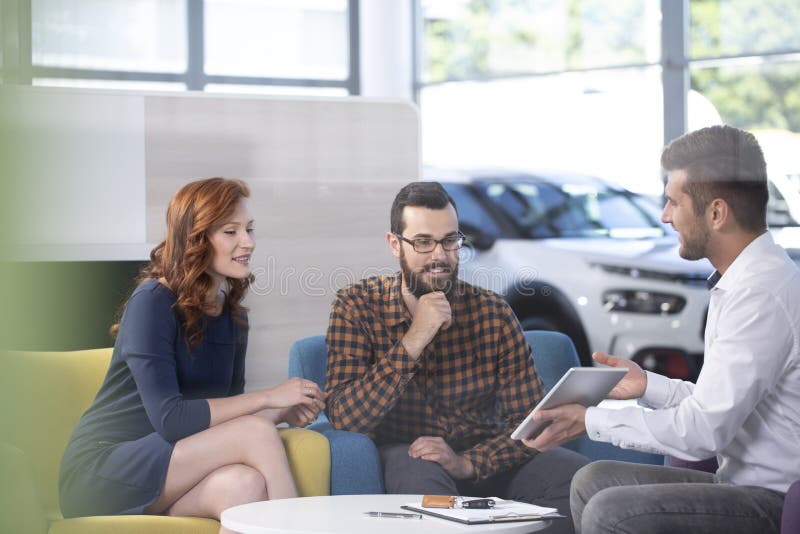 Car dealer showing an offer to his happy clients in a car showroom stock images Car dealer showing an offer to his happy clients in a car showroom stock images