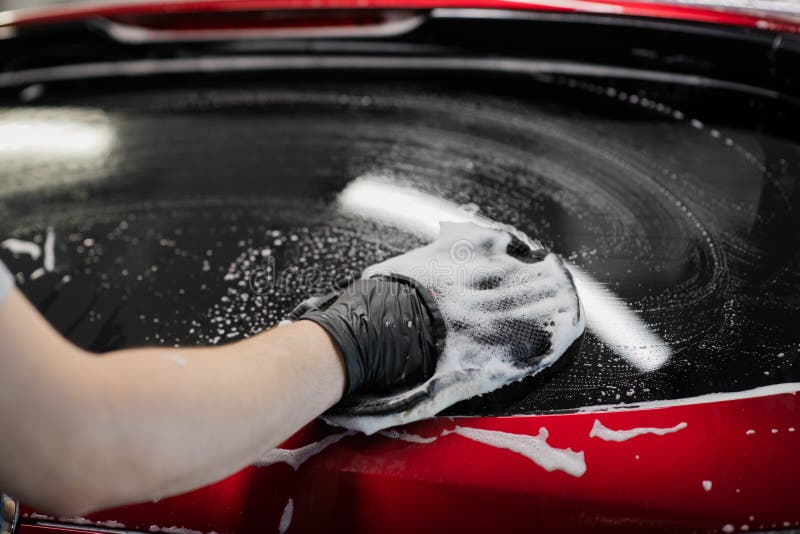 Car detailing - the man washes car with a hand covered with a special wash glove, close-up.