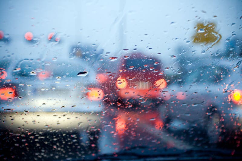 Parabrezza dell'auto con la pioggia che cade durante una tempesta, e sfocata semafori.