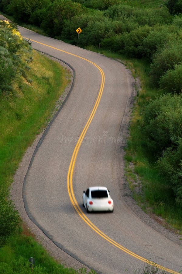 La guida in auto su strada con curvatura attraverso il verde di piante e alberi.