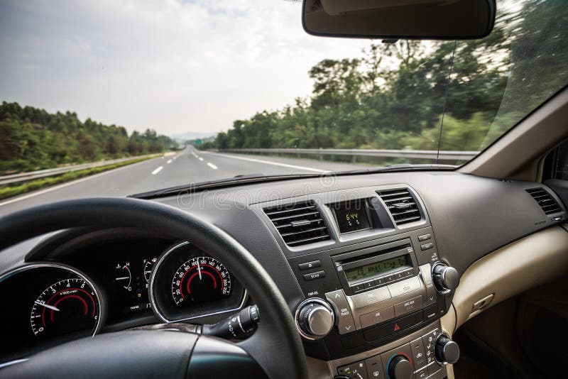 Interiér motorového vozidla pri jazde na ceste alebo diaľnici s volant a palubnú dosku v popredí.