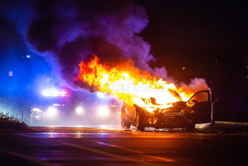 Car on Fire at Night with Police Lights in Background Editorial Photo