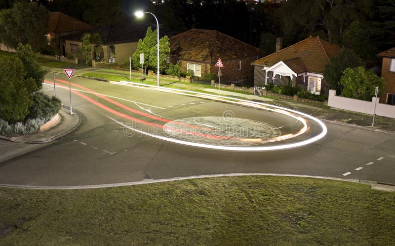 A car makes a U-turn in a round-about in a suburban built-up area, creating a light trail. A car makes a U-turn in a round-about in a suburban built-up area, creating a light trail.
