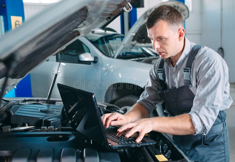 Car mechanic using a computer laptop to diagnosing and checking up on car engines parts for fixing and repair.