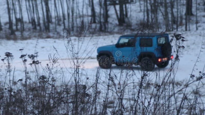 Car movement to the left. A small blue SUV is driving through the forest at off road. Winter.