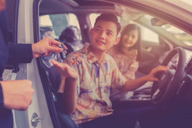 Car sales giving the key of the new car to the young attractive owners. Couple purchasing brand new car stock photo Car sales giving the key of the new car to the young attractive owners. Couple purchasing brand new car stock photo