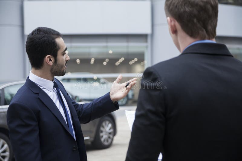 Car salesman holding car keys and selling a car to a young businessman royalty free stock photo Car salesman holding car keys and selling a car to a young businessman royalty free stock photo