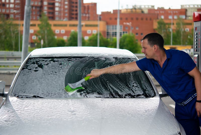 Car service worker, washes the glass with a brush with foam