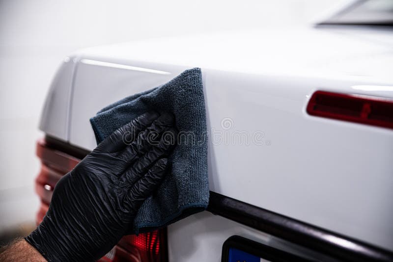 car wash or car detailing studio worker washes a white car with a cloth