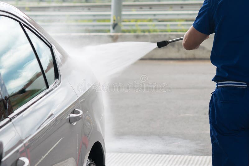 The car wash worker washes the mud with water under pressure