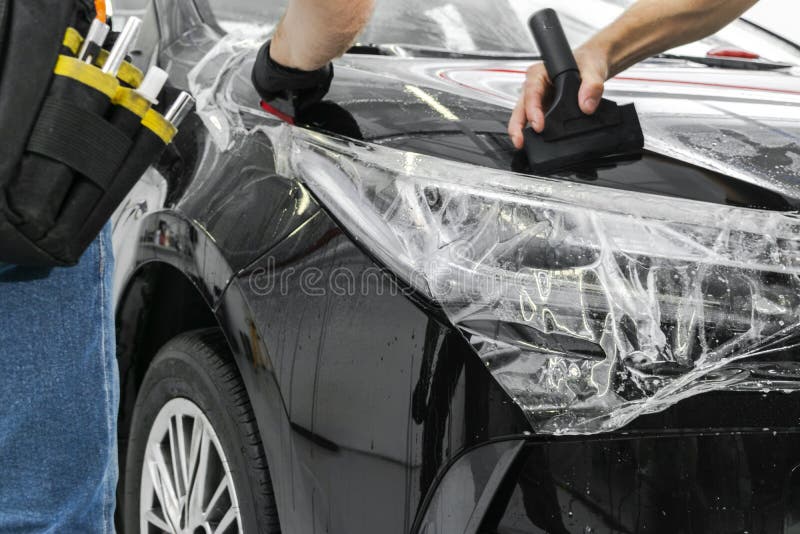 Car wrapping specialist putting vinyl foil or film on car. Protective film. Applying a protective film with tools for work. Car de