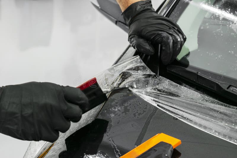 Car wrapping specialist putting vinyl foil or film on car. Protective film. Applying a protective film with tools for work. Car de