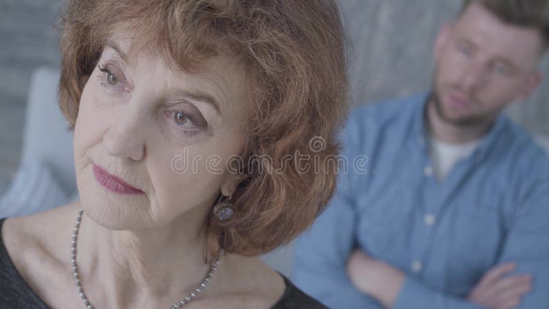 Cara ascendente cercana de una mujer triste elegante madura mayor que mira lejos en el primero plano La figura borrosa de un homb almacen de metraje de vídeo