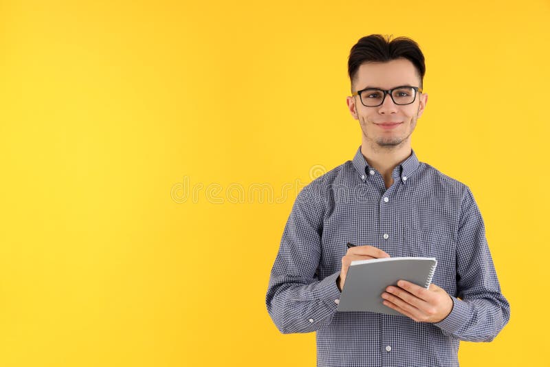 Cara atraente com notebook e caneta em fundo amarelo fotografia de stock