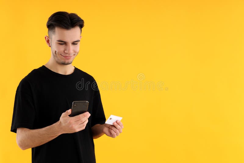 Cara com telefone e cartão de crédito em fundo amarelo imagens de stock royalty free