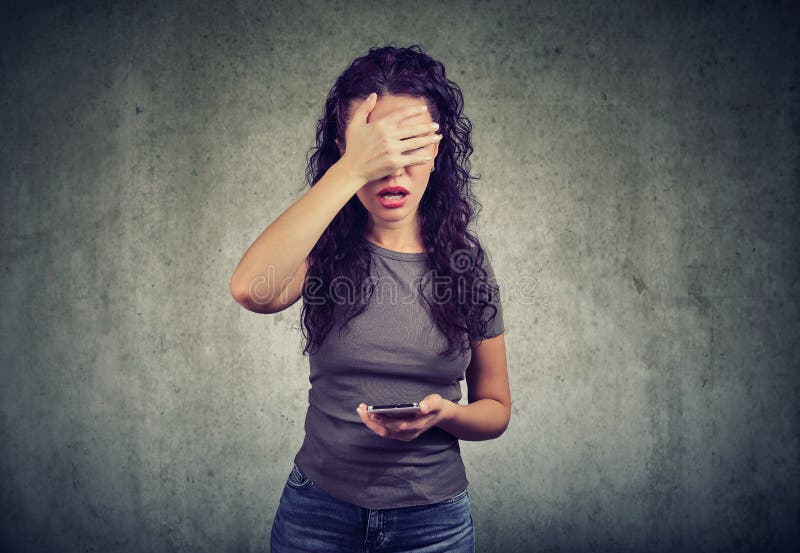 Cara de la cubierta de la mujer en la desesperación que tiene malas noticias en smartphone contra fondo gris foto de archivo libre de regalías Cara de la cubierta de la mujer en la desesperación que tiene malas noticias en smartphone contra fondo gris foto de archivo libre de regalías