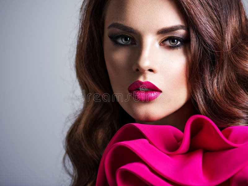 Cara del primer de una mujer hermosa con los labios rojos. La mujer joven atractiva con la cara hermosa compone con el lápiz labial rojo Retrato del primer de una muchacha elegante hermosa con el pelo rizado largo Mujer de moda en un vestido rojo con un maquillaje creativo del ojo