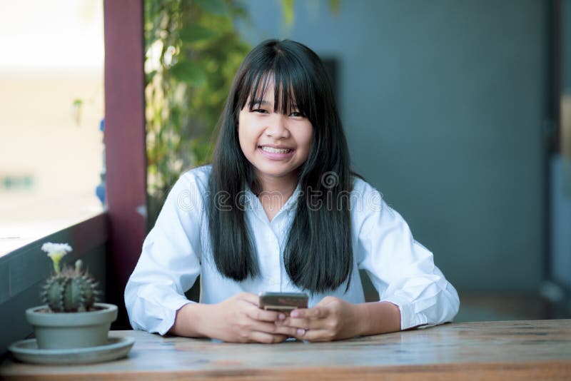 Cara sonriente toothy de un adolescente asiático con teléfono inteligente en la mano