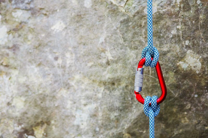 Carabiner rosso con la corda rampicante su fondo roccioso