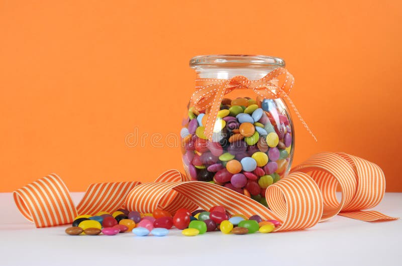 Caramelo en el tarro de cristal en fondo anaranjado y blanco fotografía de archivo Caramelo en el tarro de cristal en fondo anaranjado y blanco fotografía de archivo