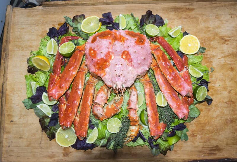 Large king crab on lettuce leaf basil herb lemon citrus limes on a wooden background. Large king crab on lettuce leaf basil herb lemon citrus limes on a wooden background