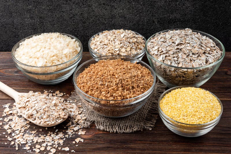 Carbohydrates. Various grain flakes in bowls on wooden. Oat, corn, rice, buckwheat, rye and wheat flakes.