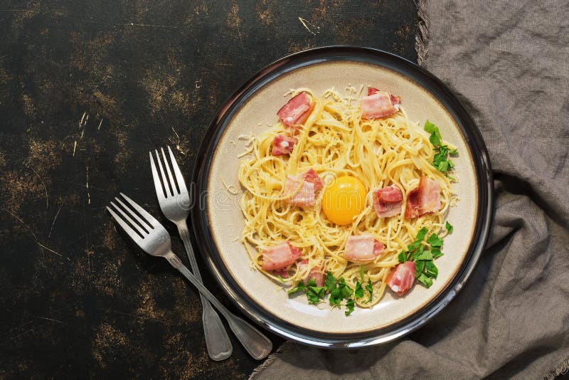 Carbonara макаронных изделий с пармезаном, беконом, сырцовым желтком на темной деревенской предпосылке над взглядом стоковое изображение rf Carbonara макаронных изделий с пармезаном, беконом, сырцовым желтком на темной деревенской предпосылке над взглядом стоковое изображение rf