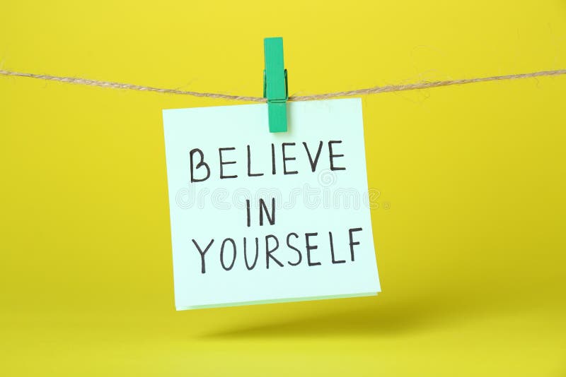 Card with phrase Believe In Yourself hanging on rope against yellow background. Motivational quote stock photo