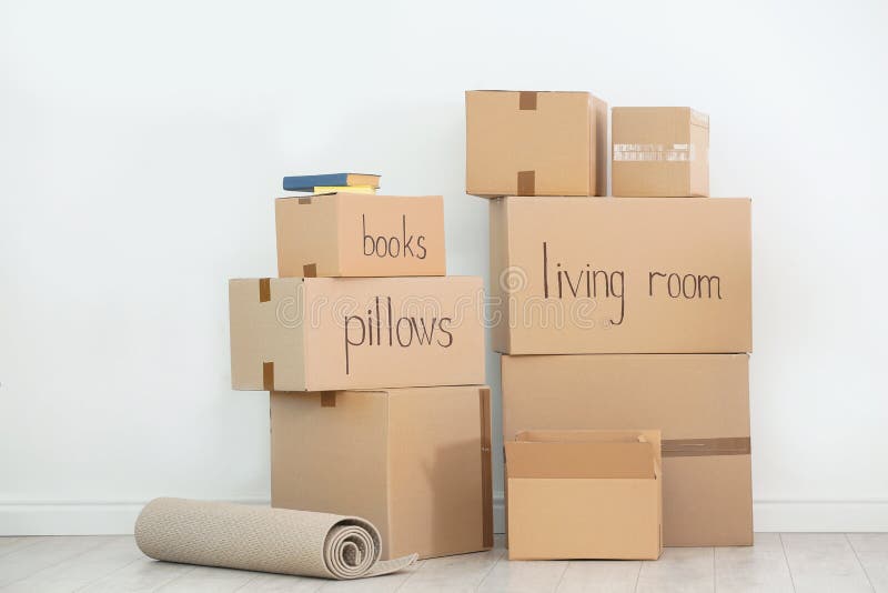 Cardboard Boxes with Books and Carpet Near White Wall Indoors. Stock