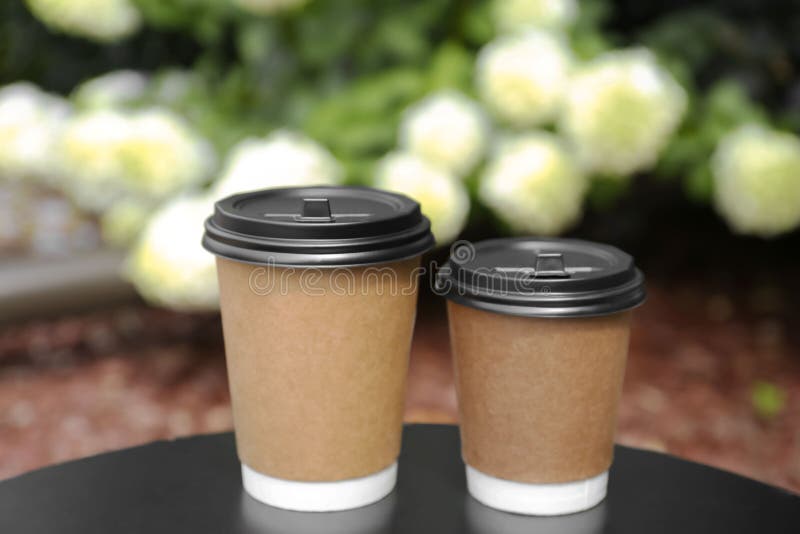 Cardboard cups with plastic lids on black table near flowers. Coffee to go stock photo