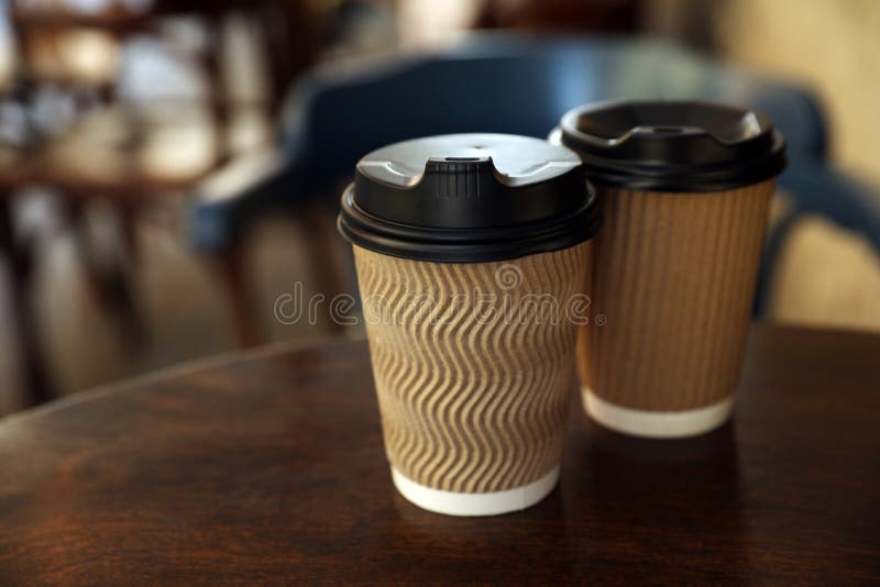 Cardboard takeaway coffee cups with plastic lids on wooden table in cafe, space for text royalty free stock photography