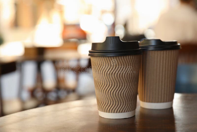 Cardboard takeaway coffee cups with plastic lids on wooden table in city, space for text royalty free stock photography
