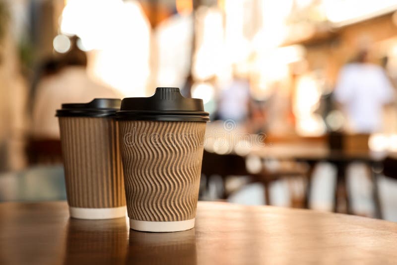 Cardboard takeaway coffee cups with plastic lids on wooden table in city, space for text stock photos