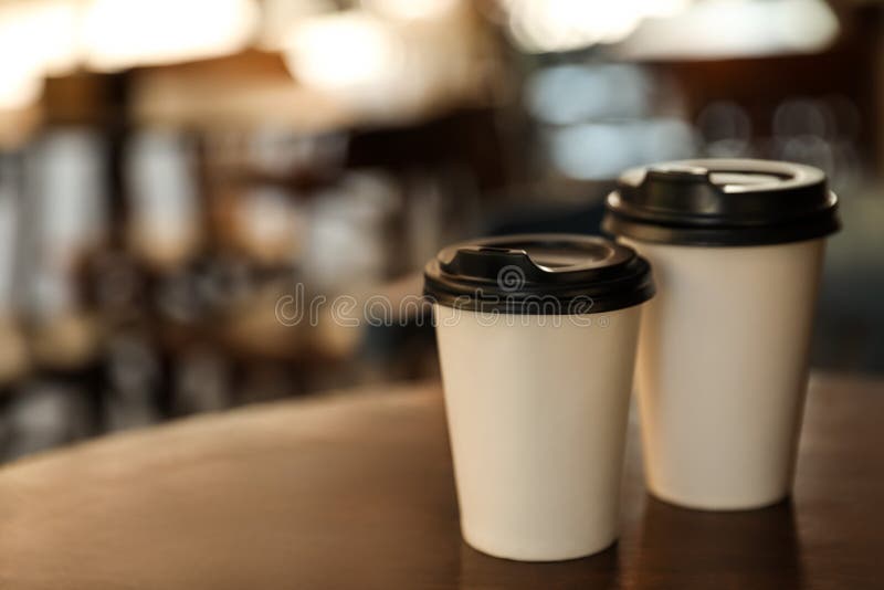 Cardboard takeaway coffee cups with plastic lids on wooden table in outdoor cafe, space for text stock photography