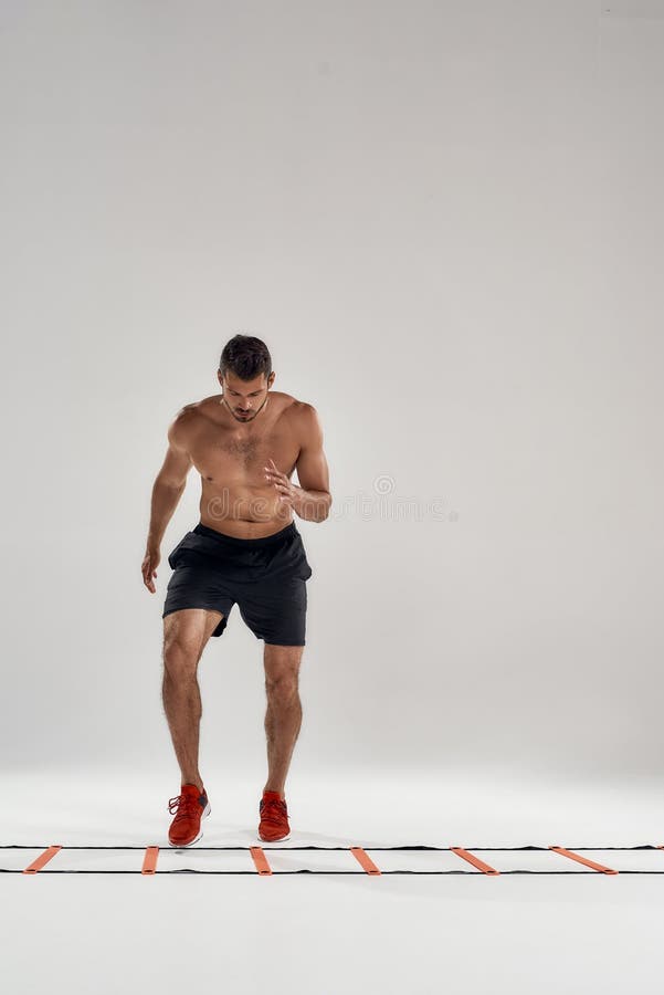 Cardio exercises. Full length shot of young athletic man training on agility ladder drill isolated over grey background