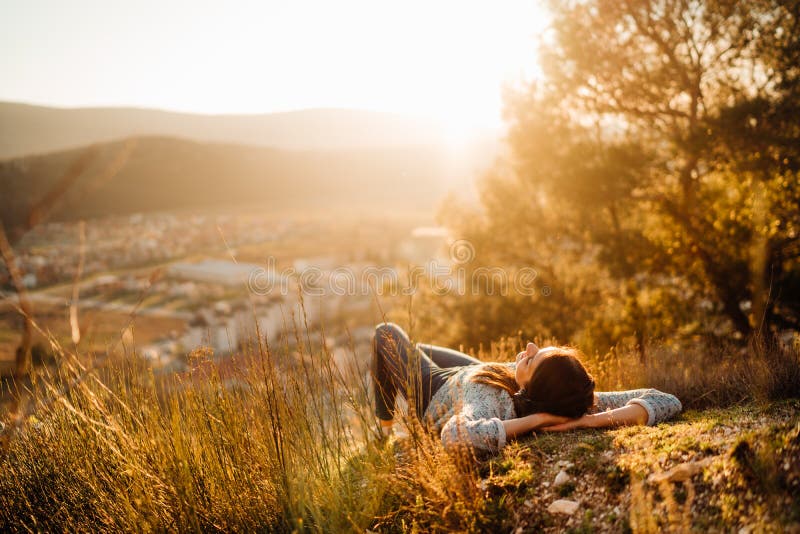 Carefree happy woman lying on green grass meadow on top of mountain enjoying sun on her face.Enjoying nature sunset.Freedom.